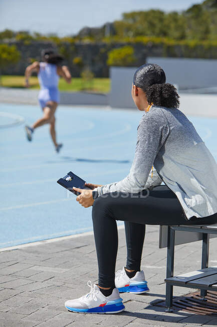 Female track and field coach watching runner on sunny track — Stock Photo
