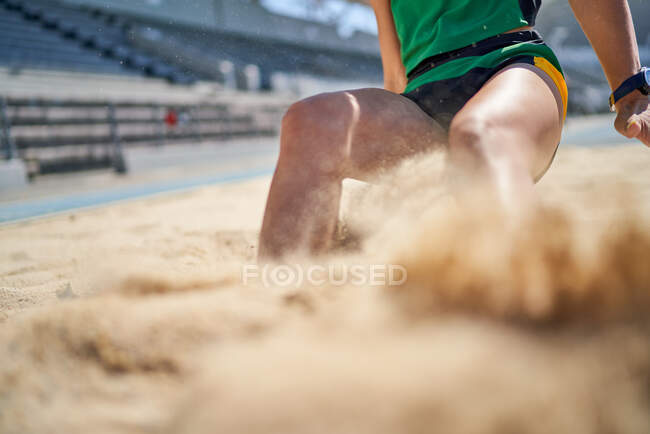 Female track and field long jumper landing in sand — Stock Photo