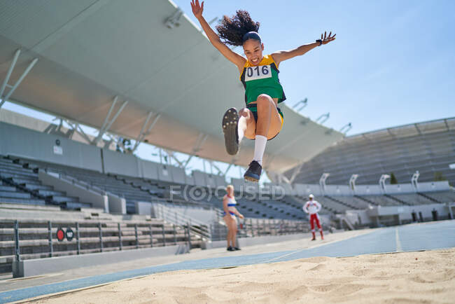 Female track and field athlete long jumping over sand — Stock Photo