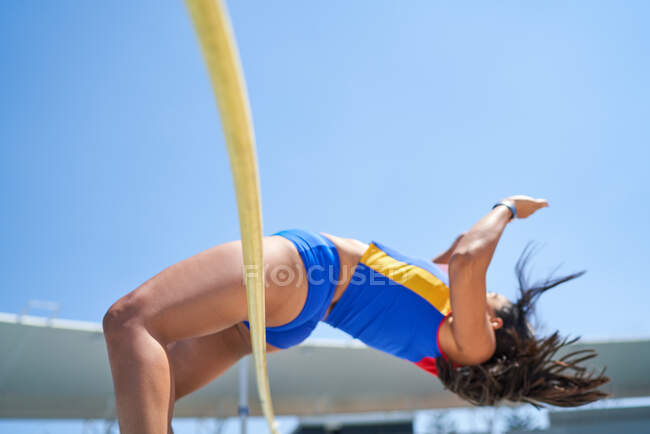Female track and field athlete high jumping over pole — Stock Photo