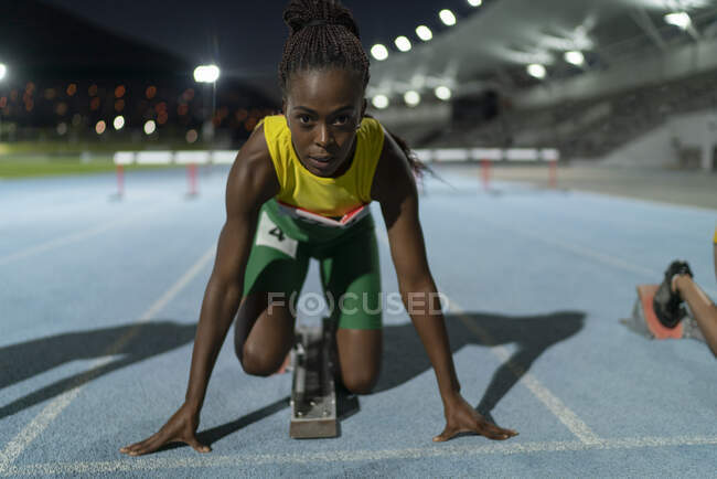 Portrait determined female track and field runner at starting block — Stock Photo