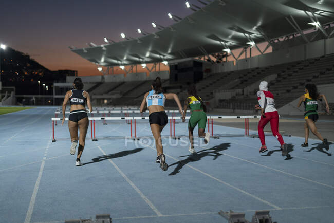 Female track and field athletes racing toward hurdles in stadium — Stock Photo