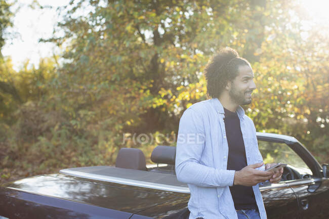 Young man with smart phone at convertible in sunny autumn park — Stock Photo