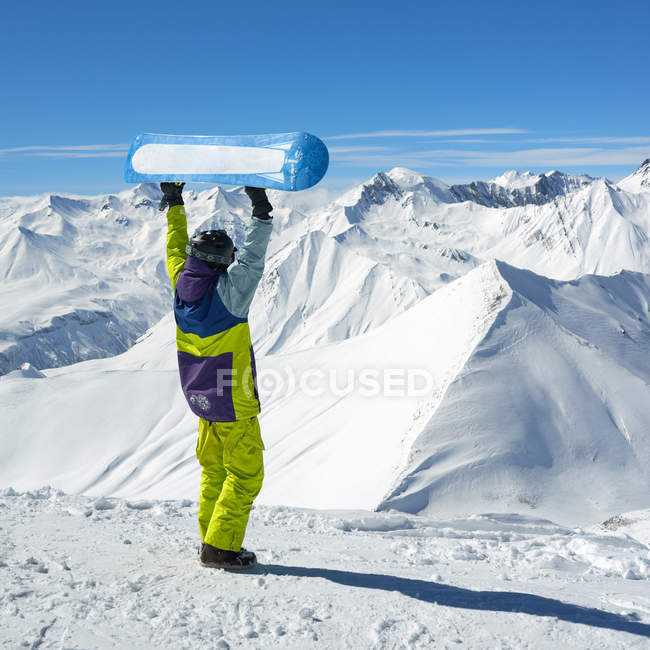 Vue arrière du snowboarder tenant la planche dans les bras levés — Photo de stock