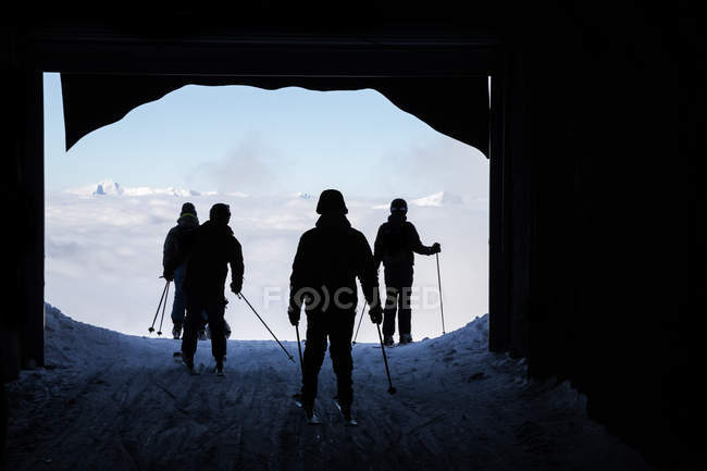 Siluetas traseras de esquiadores saliendo del túnel en las montañas - foto de stock