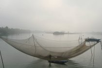 Вьетнам, Хой Ан. Человек, стоящий на лодке под рыболовной сетью — стоковое фото