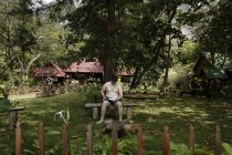 6. november 2006. thailand, krabi. Mann sitzt im Garten und liest Buch — Stockfoto