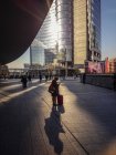 November 27, 2016. Milan, Gae Aulenti square. Woman with suitcase using mobile phone in a ray of light — Stock Photo