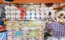 April 13, 2017. Italy, Milan. Cropped view of woman photographing stall of sweets and candies with smartphone — Stock Photo