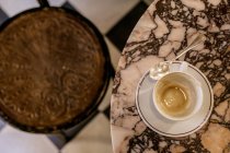 Вид зверху на каву залишається в чашці на мармуровому столі і розмитий різьблений стілець — стокове фото