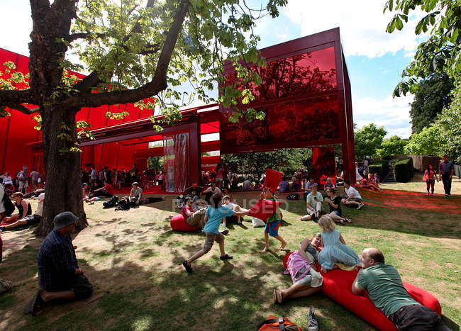24 de julio de 2010. Londres, Hyde Park, Gente descansando cerca del pabellón rojo de la galería Serpentine por Jean Nouvel - foto de stock