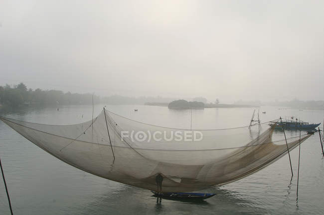 Vietnam, hoi an. Mann steht auf Boot unter Fischernetz — Stockfoto