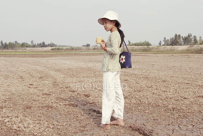 22 de marzo de 2005. Vietnam. Retrato de niña con bolso de hombro que sostiene la taza en el campo - foto de stock