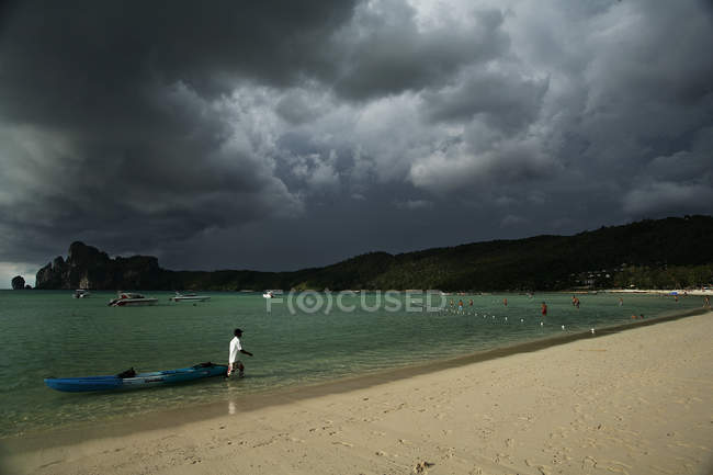 Tailandia, isla Phi Phi, bahía Loh Dalam. Hombre tirando de kayak en la orilla arenosa - foto de stock