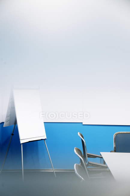 Un rotafolio en blanco con sillas y una mesa en una sala de conferencias vacía - foto de stock