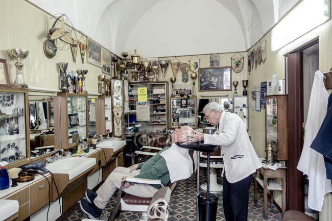 21 de abril de 2017. Apulia, Soleto. Peluquería trabajando con el cliente en barbería - foto de stock