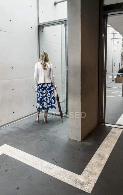 2. august 2016. deutschland, heidelberg. Hinteres Porträt einer Frau mit Regenschirm, die in der Nähe einer Glastür steht — Stockfoto