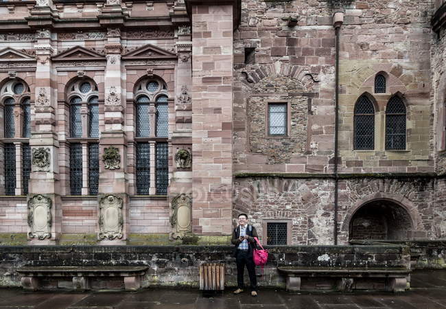 2 de agosto de 2016. Heidelberg. Asiático sorrindo homem com smartphone de pé perto do castelo — Fotografia de Stock