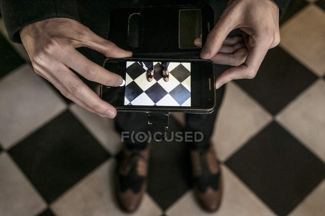 Vue recadrée de la personne photographiant ses chaussures avec un smartphone — Photo de stock