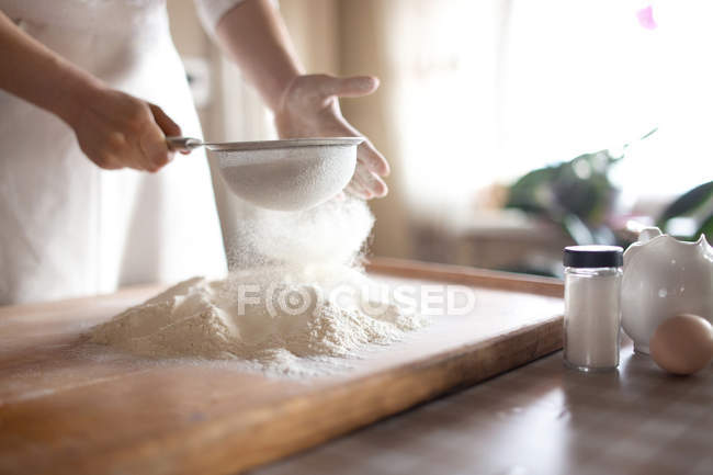 Giovane donna setacciando farina in ciotola in cucina — Foto stock