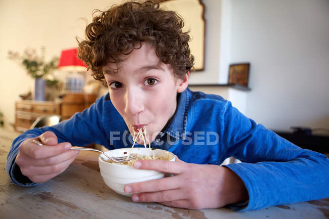 Niño feliz comiendo fideos en casa - foto de stock