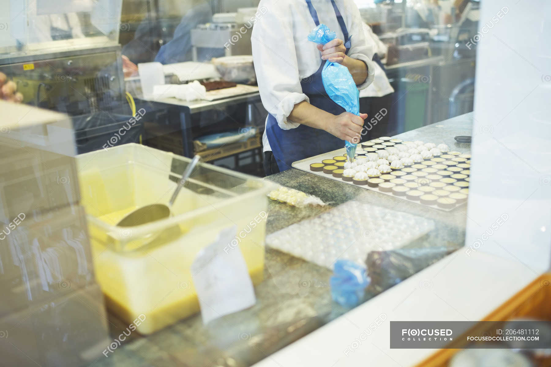 Midsection Of Female Worker Icing Sweet Food At Display Cabinet In