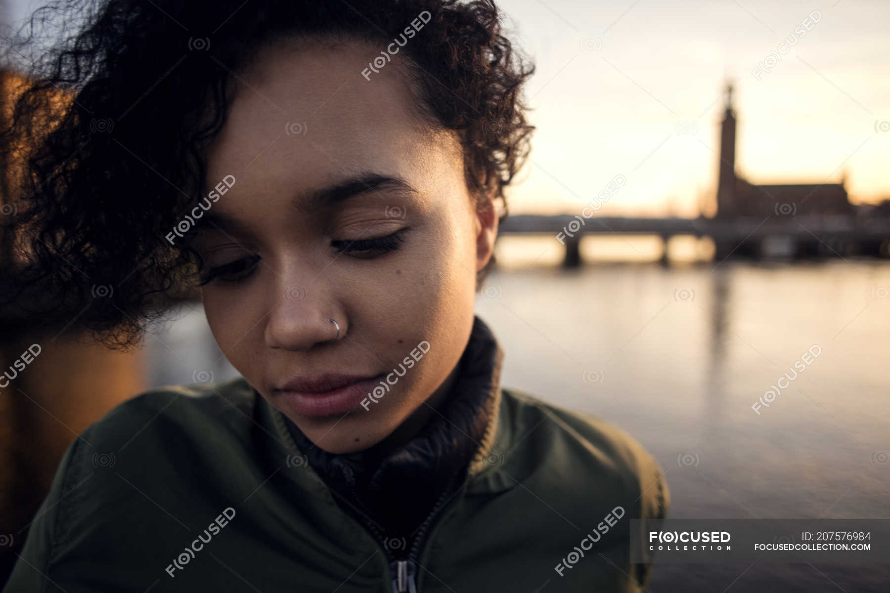 Close Up Of Teenage Girl With Curly Short Hair Looking Down While Standing Against Canal In City Sunset City Life Stock Photo 207576984