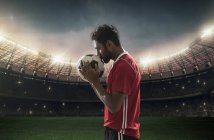 Giocatore di calcio baciare il calcio con lo stadio sullo sfondo — Foto stock