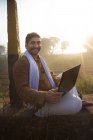 Фермер, що сидить біля сільськогосподарського поля і використовує ноутбук — стокове фото