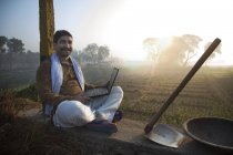 Фермер, що сидить біля сільськогосподарського поля і використовує ноутбук — стокове фото