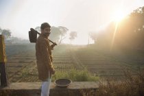 Назад вид фермера рядом с сельскохозяйственным полем с лопатой на плече против солнца — стоковое фото