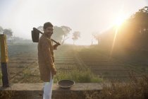 Вид ззаду фермера поблизу сільськогосподарського поля з лопатою на плечі проти сонця — стокове фото