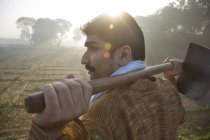 Вид ззаду фермера поблизу сільськогосподарського поля з лопатою на плечах проти сонця — стокове фото