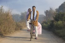 Счастливая сельская пара в традиционной одежде на велосипеде на проселочной дороге — стоковое фото