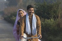 Heureux couple rural en robe traditionnelle à vélo sur la route de campagne — Photo de stock