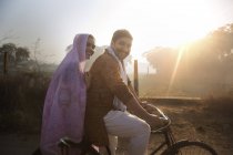 Side view of happy rural couple in traditional dress riding on bicycle at country road — Stock Photo