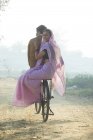Visão traseira do casal rural feliz no vestido tradicional andando de bicicleta na estrada de campo — Fotografia de Stock