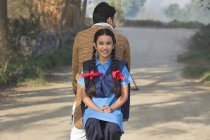 Smiling young school girl riding on bicycle along with father in village street — Stock Photo