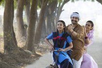 Счастливая сельская пара вместе с дочерью, катающейся на велосипеде в деревне — стоковое фото