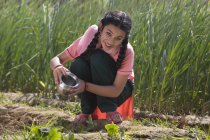 Happy Indian girl watering small plants sitting in agriculture field — Stock Photo