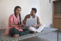 Girl sitting with father on cot and using laptop computer — Stock Photo