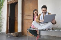 Girl sitting with father on cot and using laptop computer — Stock Photo