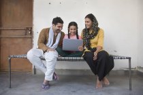 Indien fille assis avec des parents sur lit bébé et en utilisant un ordinateur portable — Photo de stock