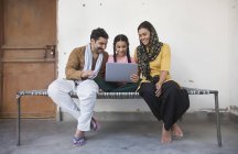 Indisches Mädchen sitzt mit Eltern auf Kinderbett und benutzt Laptop-Computer — Stockfoto