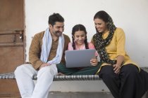 Menina indiana sentada com os pais no berço e usando computador portátil — Fotografia de Stock