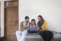 Menina indiana sentada com os pais no berço e usando computador portátil — Fotografia de Stock
