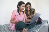 Frau sitzt mit Tochter zu Hause auf Kinderbett und benutzt Laptop — Stockfoto