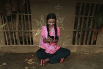 Индийская деревенская девушка сидит в сельской местности и с помощью мобильного телефона — стоковое фото