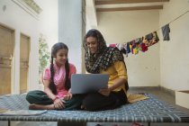 Frau sitzt mit Tochter zu Hause auf Kinderbett und benutzt Laptop — Stockfoto
