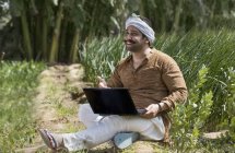Granjero indio usando computadora portátil en el campo agrícola - foto de stock